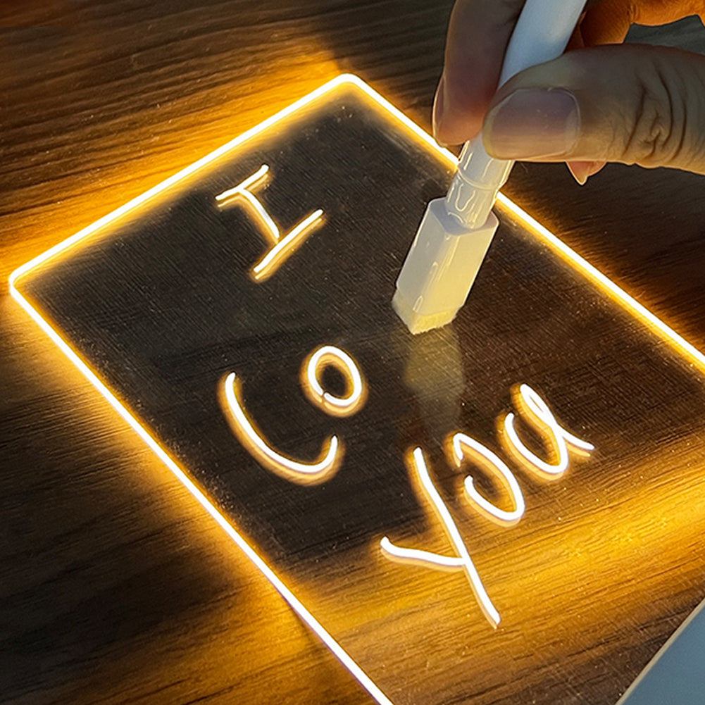 LED glow note board lit warm on a wooden desk, a hand writing a message on it with the white marker pen