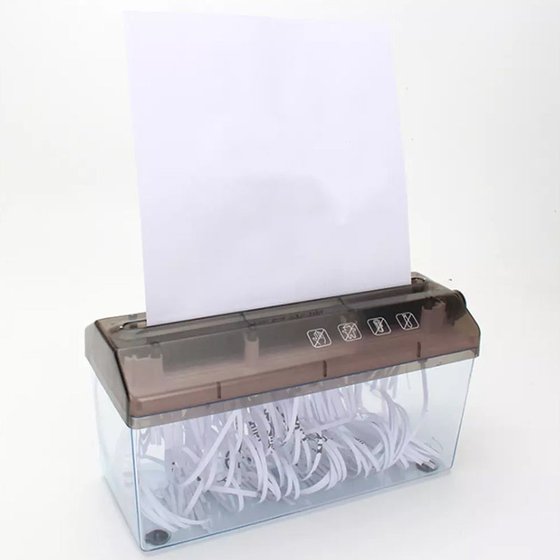 A sheet of white paper standing in the feed slot of a hand-crank paper shredder, with shredded strips collected in the clear bin below.
