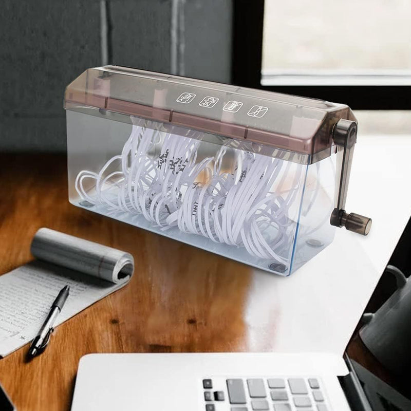 The hand-crank paper shredder on a dark wooden desk beside a notebook, a pen and a laptop.